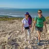Two women smiling while walking on a gravel trail with the beach in the background
