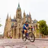 Cyclist rides across a cobblestone square in front of a Gothic cathedral featuring soaring spires, stained-glass windows, and ornate stone architecture in a historic French town.