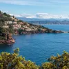 View of a bay in the French Riviera. A scenic town flows down from the hillside as blue water flows into the bay.
