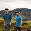 Two men smiling while walking in a valley with large mountains in the background