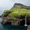 Large, grassy cliff with a waterfall and the ocean below