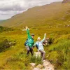 Man and woman smiling with their arms open, in the middle of a trail in the valley