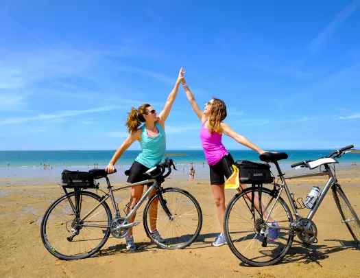 Two Backroads Guests High Fiving on Beach with Bicycles 