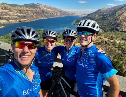 Four guests posing in front of large river/reservoir. 