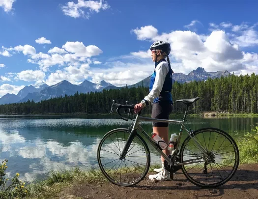 Guest standing next to bike, looking out to large lake, mountains beside them.