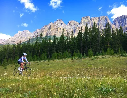Guest cycling through grassy meadow, large, craggy mountain peaks in background.