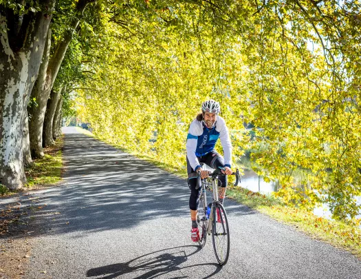 Guest/leader cycling down tree-covered road, smiling.
