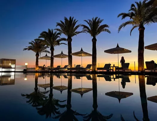 Sunset shot of still resort pool, palms, recliners.