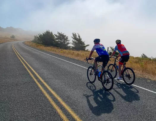 Two guests cycling up foggy road.