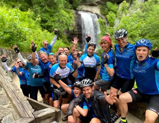 Group of guests in biking gear, waterfall behind them.