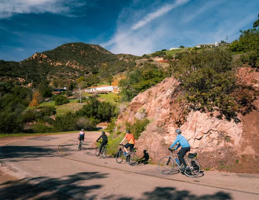 Four guests rounding a corner, hilltop houses and Cali hills in background.