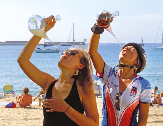 Two guests on beach, drinking from ornate wine glasses.