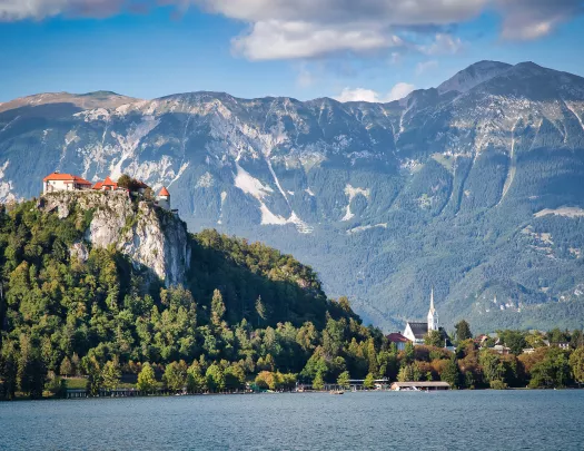 Wide shot of Bled Castle, town, lake below, mountain behind.