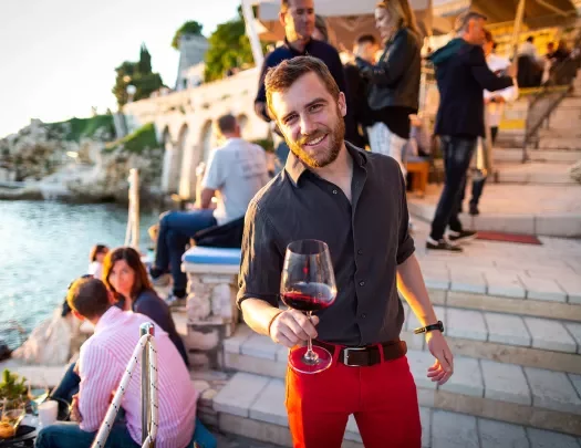 Man among group of other people, wine glass in hand, sunset.