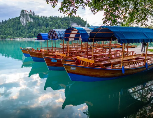 Four wooen, boats on blue lake, hills, castle in distance.