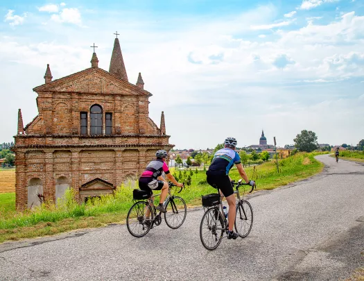 Cyclists riding along an Italian road with an old church building