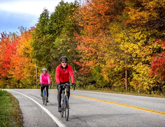 Two guests cycling down road, fall-colored trees to their left.