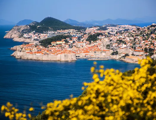 Wide shot of Dubrovnik coastline, blue ocean, white and tan houses.