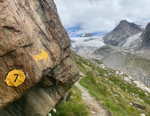 Painted trail marker on side of cliff, hiking trail in distance.
