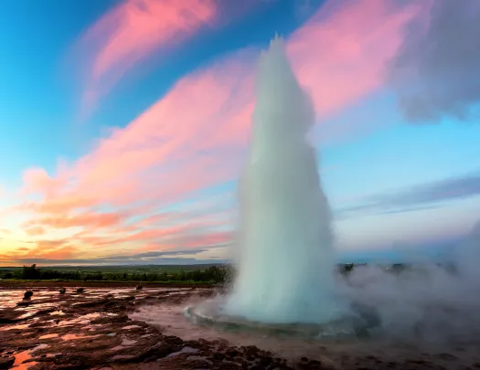 Shot of thermal geyser erupting, vibrant pink/blue sunset.