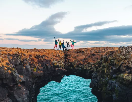 Guests posing on rock archway above ocean
