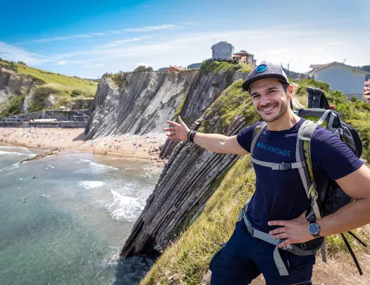 Leader gesturing to craggy cliffs, large beach, buildings dotting cliffside.