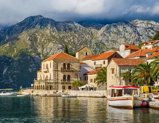 Shot of Croatian houses on coast, boats, mountain in distance.