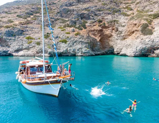 Guests near and on boat, swimming, relaxing, rocky coast nearby.