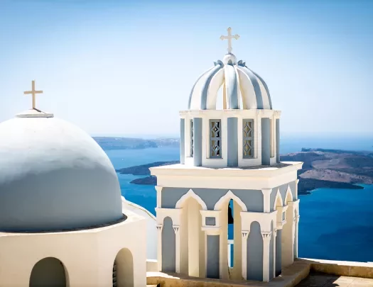 Close up of blue domes of Santorini, ocean behind them.