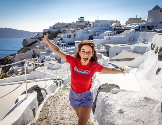 Guest emoting to camera, white walled coastal buildings behind her.