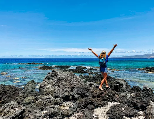 Woman walking towards the ocean with her arms in the air