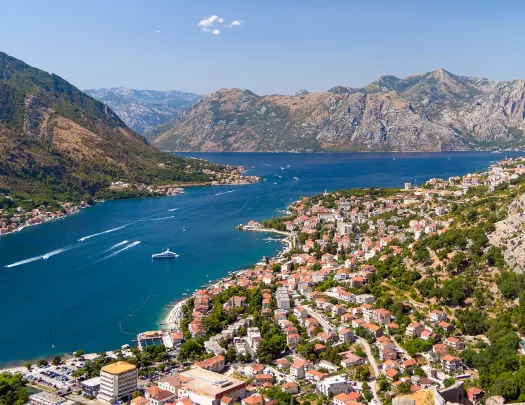Bird's eye of Croatian riverside city, mountains all around, boats in river.