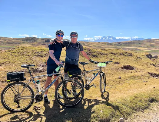 Two guests with bikes on golden meadow, mountains behind them.