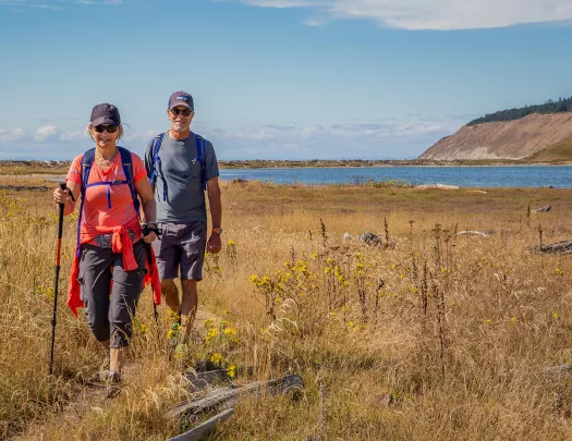 Two guests walking through grassy coast, ocean, cliffside behind them.