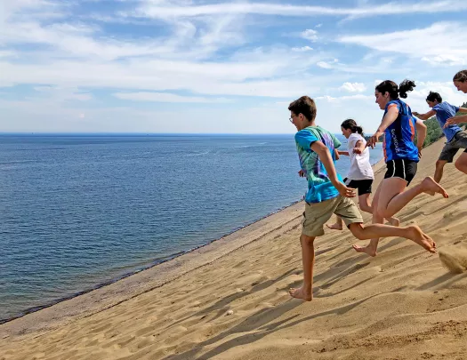 Group of young guests running down sand dune towards ocean.