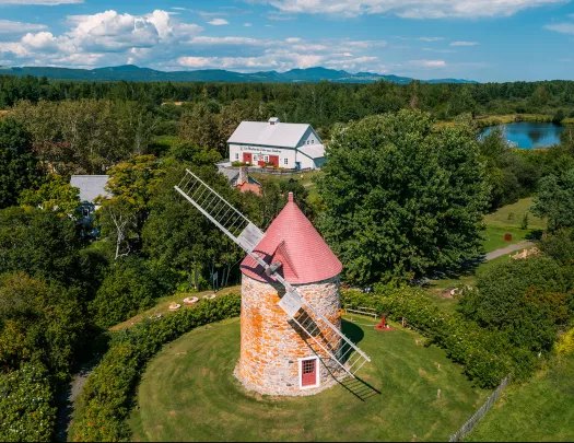 Wide shot of large windmill, white building in background.