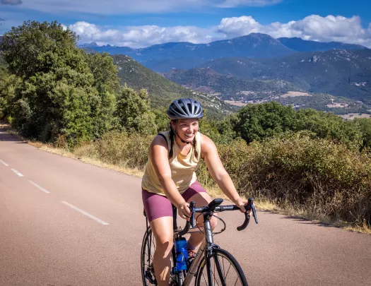 Guest cycling down road, hills and mountains in background.