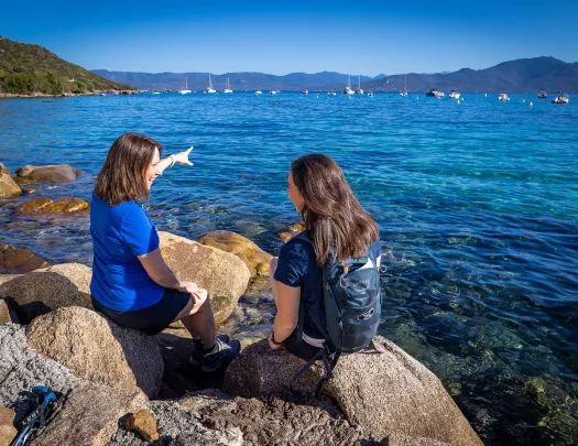 Two guests sitting on large rocks on coast, one pointing towards ocean.