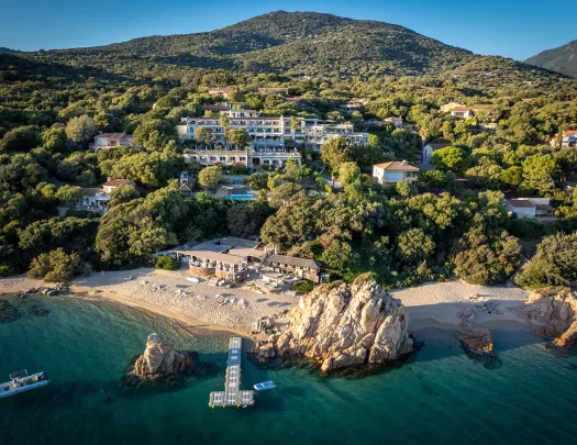 Wide shot of a large hotel in the hillside, beach, small boats and ocean in foreground.