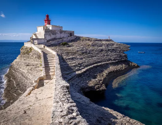 Point of view shot of a rocky trail leading towards a small lighthouse.