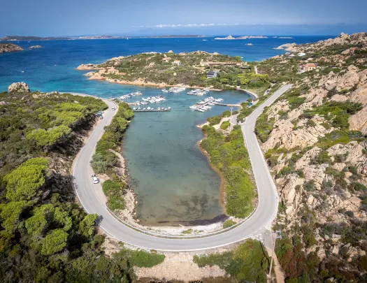 Bird's eye shot of a "U" shaped road on the Italian coastline, small boats and piers in distance.