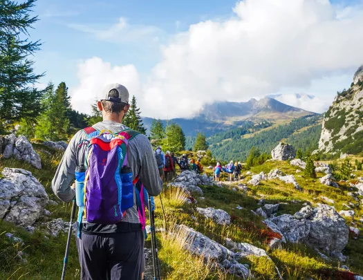 Group of guests hiking down mountain trail, cloudy mountainous vista in distance.