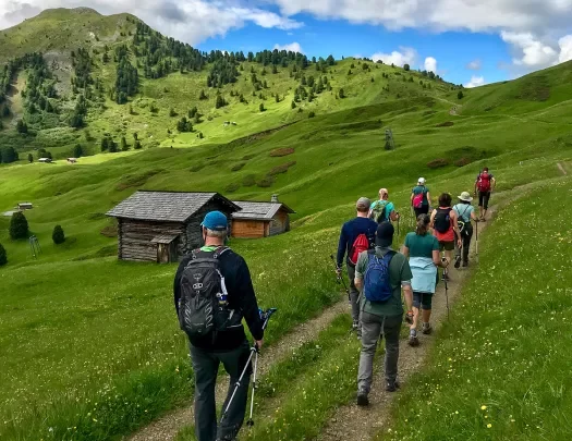 Group of guests hiking in meadow, two small wooden shacks to their left.