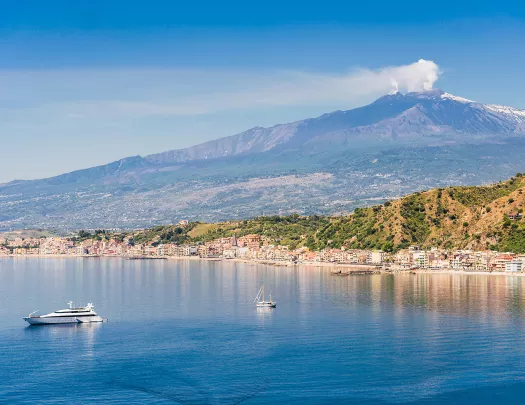 Wide shot of Mount Etna, small boats in water in foreground.