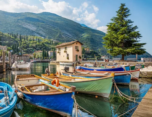 Small coastal pier, colorful ships visible, mountain in distance.