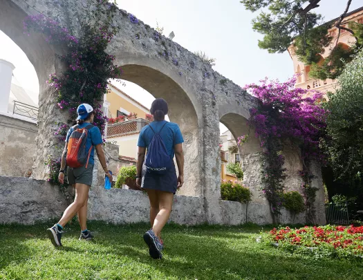 Two guests walking through arched garden. Red and purple flowers.