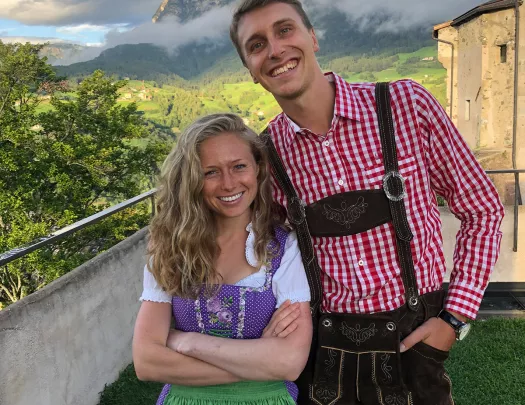 Two locals smiling, large mountains, clouds behind them.