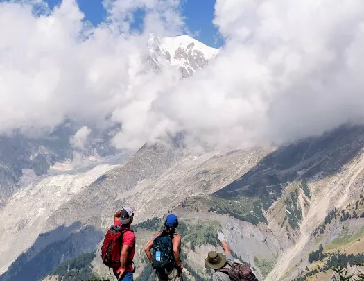 Three guests on hillside, one pointing towards distant mountain.