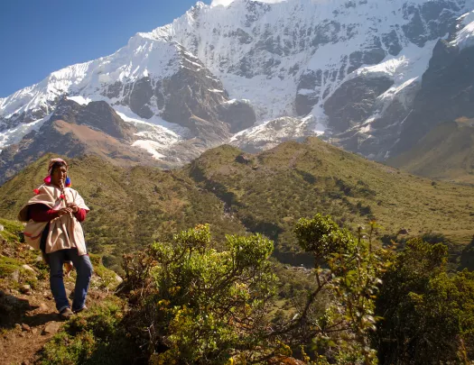 Local on hillside playing instrument, snowy mountains, hills behind them.