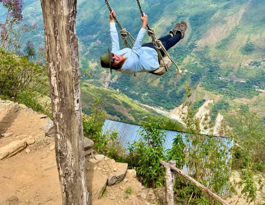 Guest on cliffside swing, overlooking large drop.